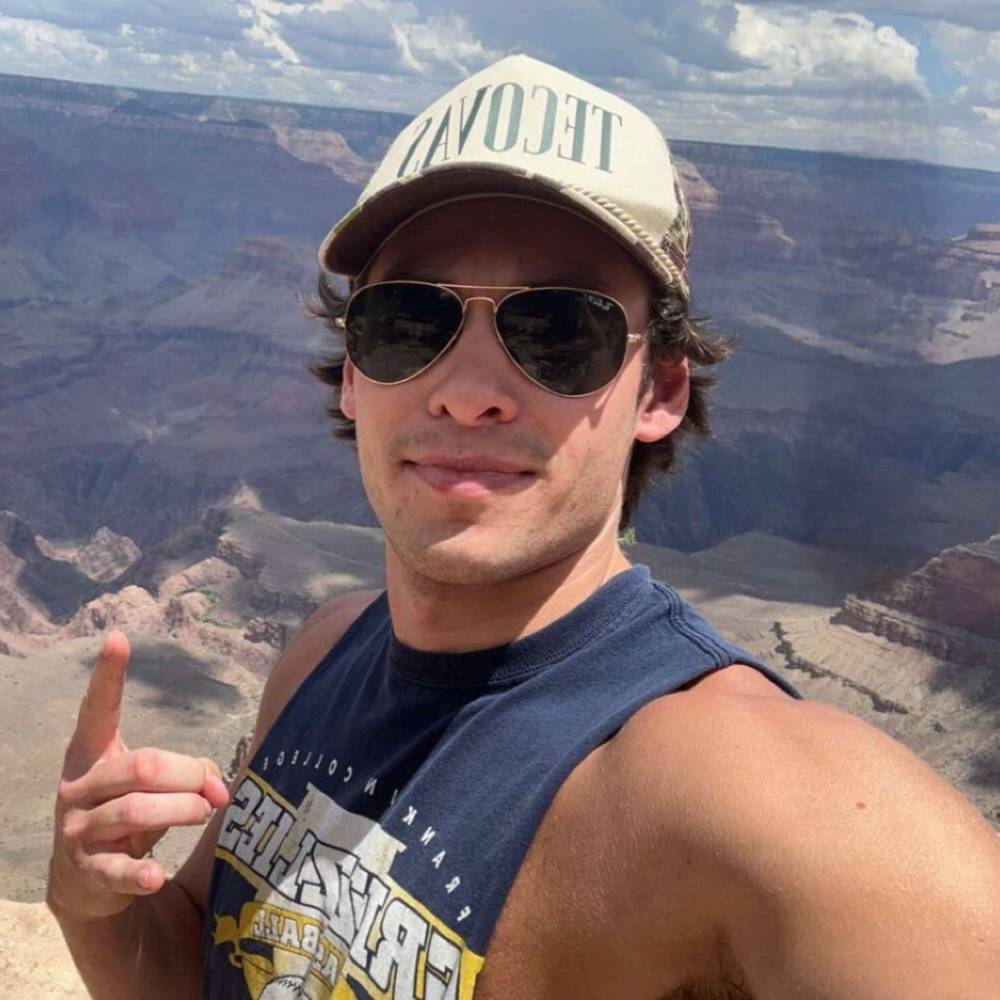 a man wearing sunglasses and standing in front of a mountain